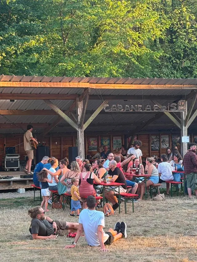 Le public assis dans l'herbe devant la scène de la cabane